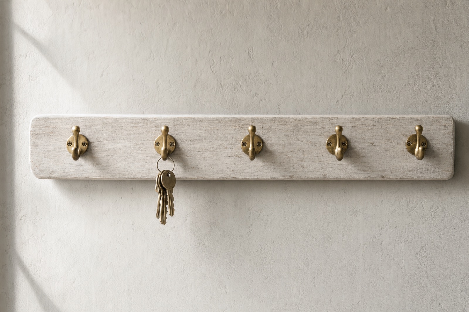 A row of brass hooks on a timber rail, the first hook empty and a set of keys hanging on the second.